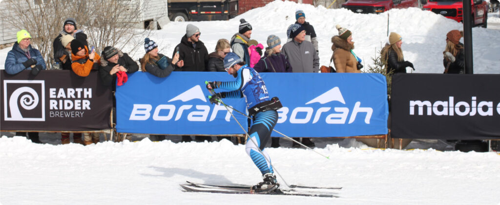 Birkie skier racing towards the finish line, in the background two blue Borah Teamwear barrier banners.