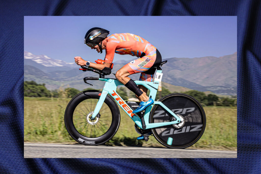 Triathlete riding a bicycle hard hunched over in the aero position position wearing a colorful custom cycling kit.